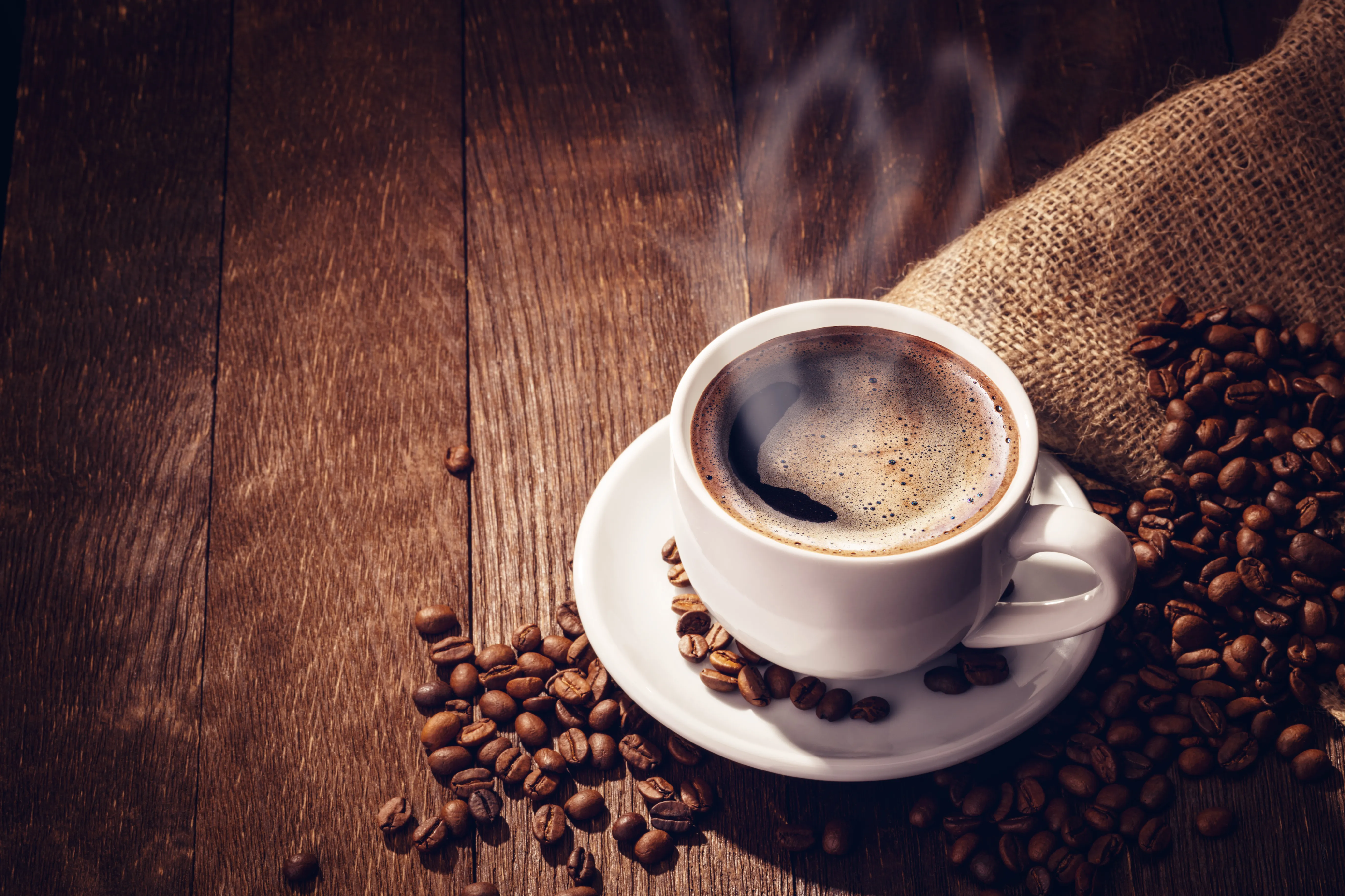 A steaming cup of coffee with roasted beans in a burlap sack